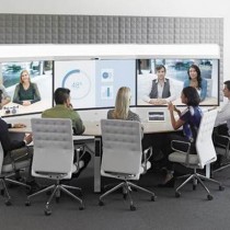 Cisco IX5000 Immersive Telepresence Suite in use. 3 screens, middle with data, 6 grey chairs close side of oval table.